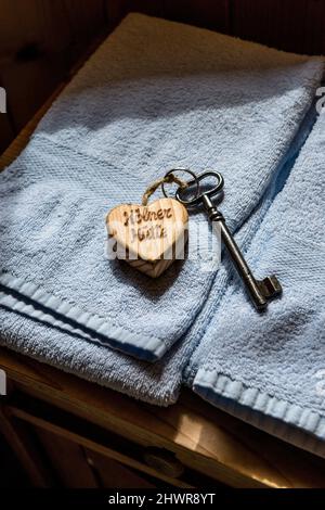 Vecchia chiave della casa sul portachiavi a forma di cuore che giace sulla parte superiore di asciugamani blu pastello Foto Stock
