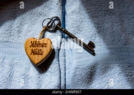 Vecchia chiave della casa sul portachiavi a forma di cuore che giace sulla parte superiore di asciugamani blu pastello Foto Stock
