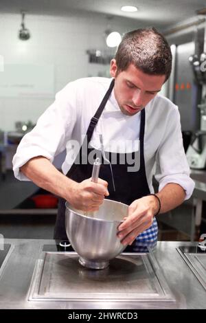 HES un artista in cucina. Uno chef prepara con cura un pasto gourmet. Foto Stock