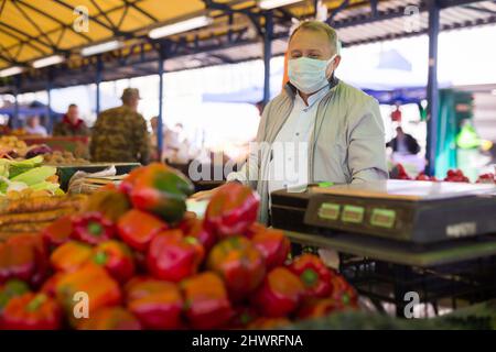 Uomo in maschera acquistare pepe nel mercato Foto Stock