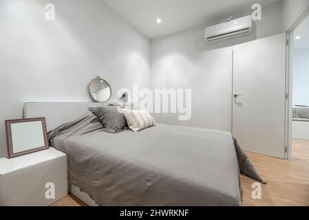 Camera da letto con letto king size con copriletto grigio, cuscini, specchio rotondo e aria condizionata Foto Stock