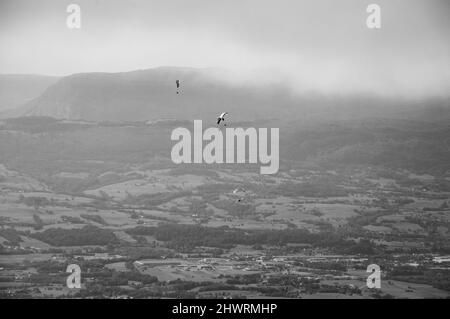 I parapendio sorvolano le montagne della valle e delle Alpi sullo sfondo. Zona del lago di Annecy (alta Savoia, Francia). Foto invecchiata. Bianco e nero. Foto Stock