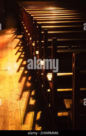 File di banchi di chiesa. Luce solare filtrata attraverso la vetrata colorata. Messa a fuoco selettiva. Foto Stock