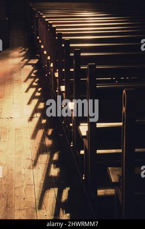 File di banchi di chiesa. Luce solare filtrata attraverso la vetrata colorata. Messa a fuoco selettiva. Foto storica di Seppia Foto Stock