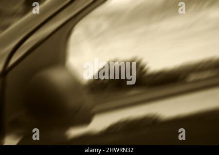 Foto sfocata del paesaggio rurale riflessa nella finestra laterale di un'auto. Foto astratta di seppia. Foto Stock