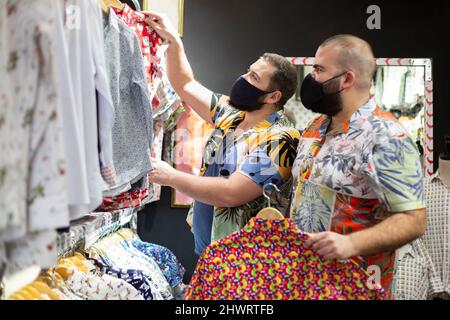 Coppia gay con maschera di acquisto vestiti all'interno di un negozio di magliette. Foto Stock