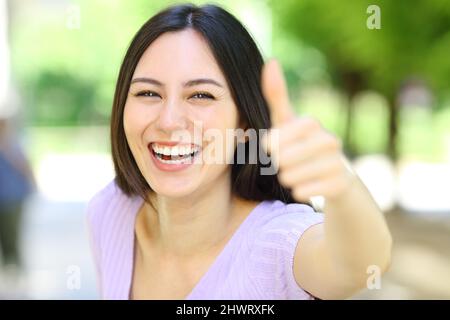 Vista frontale ritratto di una donna asiatica felice gesturando pollice in su in un parco Foto Stock