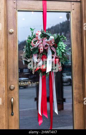 Una corona di Natale con nastro appeso da una porta d'ingresso in vetro come arredamento invernale dicembre all'aperto Foto Stock