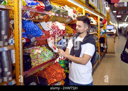 Cliente presso il negozio DIY in piedi vicino allo scaffale con guanti di gomma e un paio di indossare Foto Stock