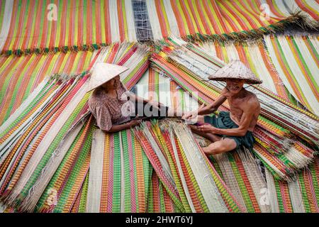 Vietnamita Old Man e le donne che fanno un asciugando tradizionale vietnam stuoie nel vecchio villaggio tradizionale a dinh Yen, dong thap, vietnam, artista di tradizione Foto Stock