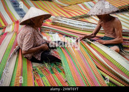 Vietnamita Old Man e le donne che fanno un asciugando tradizionale vietnam stuoie nel vecchio villaggio tradizionale a dinh Yen, dong thap, vietnam, artista di tradizione Foto Stock