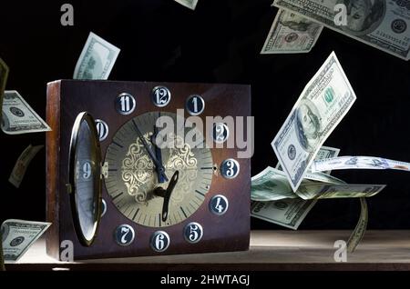 Orologio meccanico da tavolo e denaro. Orologio con frecce e denaro fluttuante. Tempo di partenza. Tempo prezioso. Vista frontale. Foto Stock