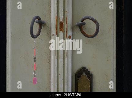 Vecchia casa rurale invecchiato porta d'ingresso in legno con due antichi ganci arrugginiti e una mano fatta appendere perline fascino fortunato a Nafplio, Grecia. Foto Stock