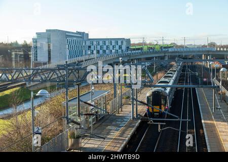 La vista dalla stazione ferroviaria di Edinburgh Park di un treno nella stazione e di un tram sul cavalcavia, Edimburgo Foto Stock