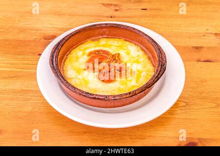 Gran receta italiana para una porción de queso provolone a la parrilla en una olla de barro con tomate y pimiento picado en el centro de la comida Foto Stock