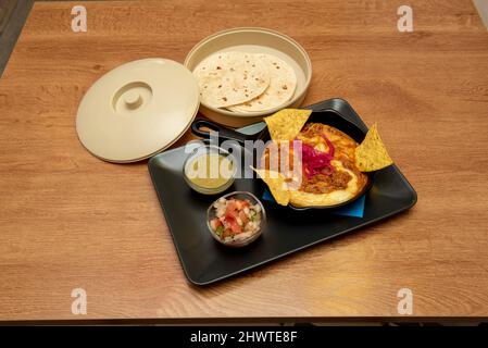 Cochinita pibil taco su un letto di formaggio fuso con salsa al peperoncino e pico de gallo e una teglia con tortilla di grano Foto Stock
