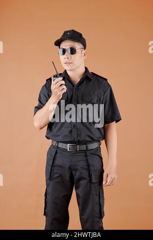 Ritratto di guardia di sicurezza maschile in occhiali da sole che parlano su walkie-talkie con collega Foto Stock