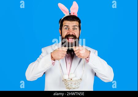 Tradizione e simbolo pasquale. Felice uomo Bearded in orecchie conigliate con uova di cestino. Preparazione per la Pasqua. Foto Stock