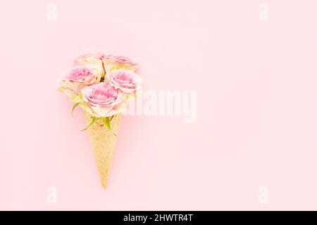 Rose rosa in un cono di gelato a base di waffle su sfondo rosa. Festa delle madri, giorno di San Valentino, bachelorette, concetto estivo. Spazio di copia, vista dall'alto Foto Stock