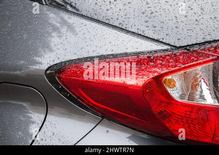 Retroilluminazione rossa brillante per auto coperta da gocce di pioggia e carrozzeria lucida in grigio neutro Foto Stock