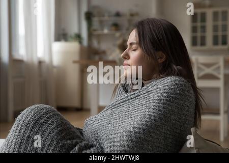 Donna coperta in calda plaid seduta sul divano a casa Foto Stock