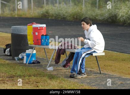 Partita di calcio di 11 e 12 anni giocatori che stanno perdendo e la stella QB è ferita e seduta sul banco di osservazione e non fare nulla per aiutare Foto Stock