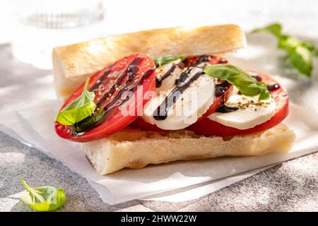 Delizioso panino con insalata caprese. Pomodori maturi e mozzarella con foglie di basilico fresco. Cucina italiana. Foto Stock