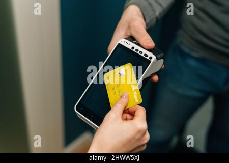 Primo piano corto scatto di corriere maschio irriconoscibile dando terminale wireless POS a fare il pagamento contactless via carta di credito a giovane femmina Foto Stock