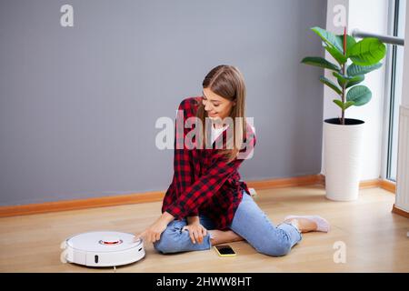 Donna accende l'aspirapolvere robot intelligente Foto Stock
