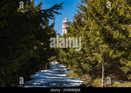 OWL Mountains, Polonia - Aprile 2021: Lungo sentiero innevato fino alla vetta più alta delle montagne Owl Great Owl con vista sulla parte superiore della torre panoramica in cima Foto Stock