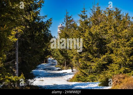 OWL Mountains, Polonia - Aprile 2021: Lungo sentiero innevato fino alla vetta più alta delle montagne Owl Great Owl con vista sulla parte superiore della torre panoramica in cima Foto Stock