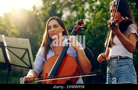 Ha insegnato a sua figlia come giocare. Scatto corto di una madre e di una figlia che suonano strumenti musicali insieme nel cortile. Foto Stock