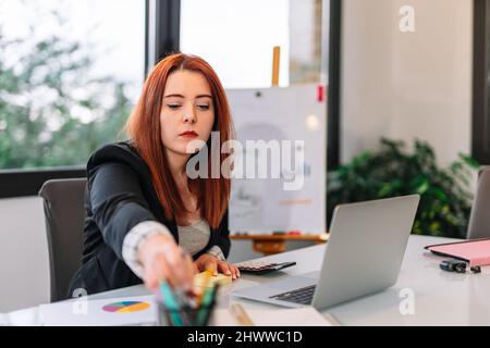 Giovane imprenditore telelavoro a casa. Prendere una penna mentre si prendono appunti dal computer. Foto Stock