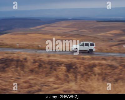 SUV corre sulla strada circondata da campi e colline. Immagine sfocata. Paesaggio del Caucaso settentrionale Foto Stock