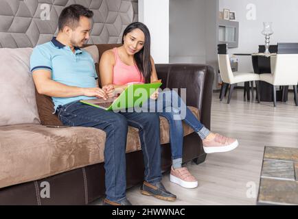 L'uomo e la donna che effettuano gli acquisti in linea dal loro calcolatore con la loro carta di credito nel soggiorno della loro casa Foto Stock