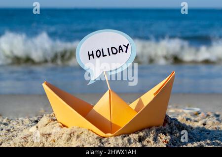 Orange Paper Boat su Sandy Seashore Close-up. Piccola barca da carta Foto Stock