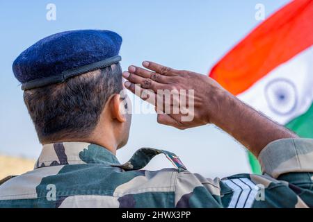 Back view shot di orgoglioso militare indiano saluta osservando bandiera indiana - concetto di patriota, nazionalismo e onore Foto Stock