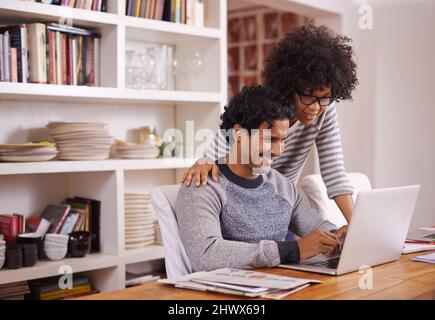 Rimanere connessi. Scatto di una giovane coppia usando un computer portatile insieme a casa. Foto Stock