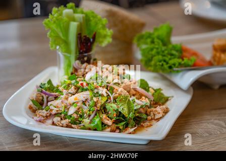 Primo piano Larb Moo o insalata di maiale speziata sminuzzata servita con verdure fresche, il tradizionale popolare cibo speziato thailandese del nord, Thailandia. Cibo in whit Foto Stock