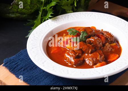 Concetto di cibo fatto in casa Francese Stew Beef Marengo in ceramica bianca piatto zuppa su asse di legno su sfondo nero ardesia pietra con spazio copia Foto Stock