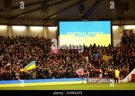 Nottingham, Regno Unito. 07th Mar 2022. Il calcio si leva insieme sul grande schermo, mentre un ventilatore della Foresta ondeggia una bandiera Ucraina alla foresta di Nottingham contro Huddersfield Town, partita di round della fa Cup di Emirates 5th, al terreno della città, Nottingham, Notts. Credit: Paul Marriott/Alamy Live News Foto Stock