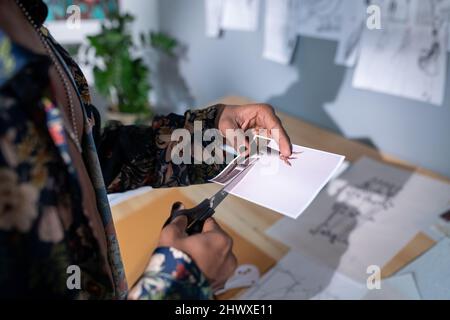 Mani di giovane uomo creativo con le unghie lucidate che tagliano fuori la foto con il vaso mentre andando fare la composizione o il collage dell'arte Foto Stock