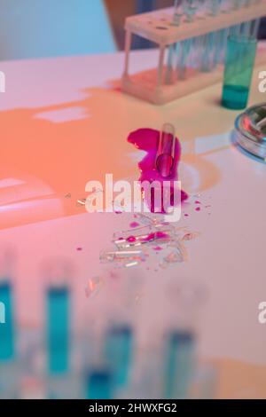 Barattoni di vetro rotto con sostanza chimica pericolosa di colore viola sul posto di lavoro dello scienziato in laboratorio moderno Foto Stock