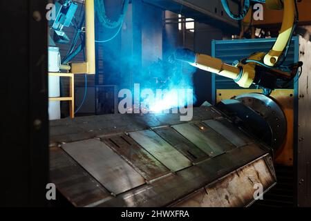 Processo di saldatura ad arco prodotto da un'enorme macchina industriale robotica in una grande officina di fabbriche o impianti contemporanei Foto Stock