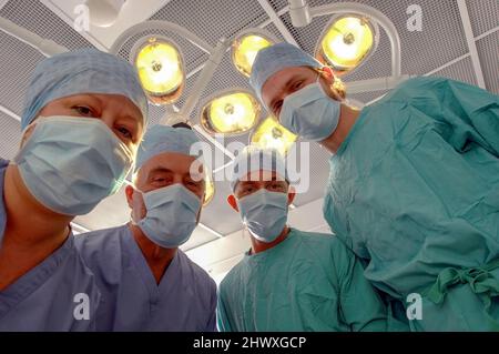 Vista del paziente di un team di chirurghi mascherati sotto le luci di un teatro operatorio ospedaliero (MODELLO RILASCIATO). Foto Stock