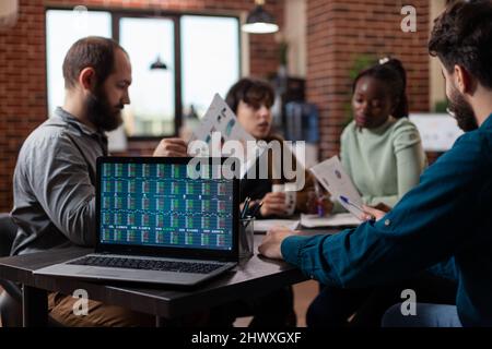 Diversi uomini d'affari che discutono di profitto finanziario che analizzano i dati di stock durante la riunione di affari nell'ufficio di startup. Computer portatile con rapporto annuale sullo schermo del computer. Economia globale Foto Stock