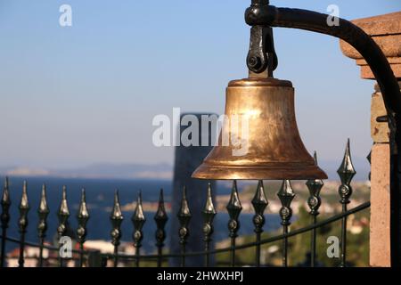 Vecchia campana di bronzo sul muro. Campana d'oro storica. Una campana e vista mare e paesaggio alle sue spalle. Campana della Chiesa. Foto Stock