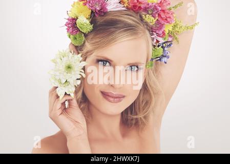 Sentirsi come una dea primaverile. Una giovane donna con una disposizione di fiori nei suoi capelli sorridendo alla macchina fotografica. Foto Stock