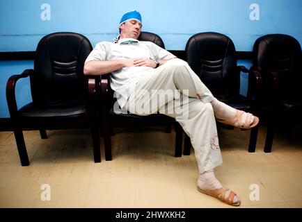 Un membro del personale del teatro dorme su una sedia nella sala d'attesa del personale dell'ospedale.(MODELLO RILASCIATO) Foto Stock