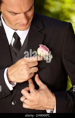 Preparazione dell'ultimo minuto. Bel giovane sposo che regola il suo boutonniere. Foto Stock